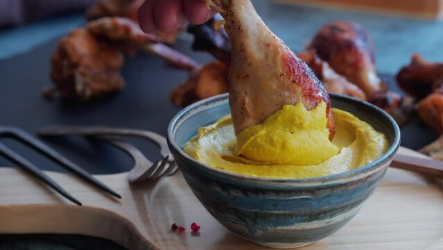 Bowl of tasty mustard sauce with grilled chicken wings and drumsticks
