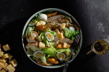 Caesar salad with chicken in a plate on a dark background