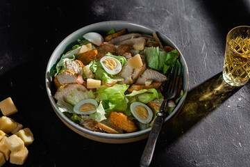 Caesar salad with chicken in a plate on a dark background