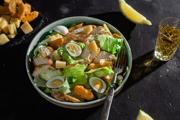 Caesar salad with chicken in a plate on a dark background