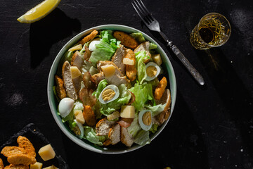 Caesar salad with chicken in a plate on a dark background