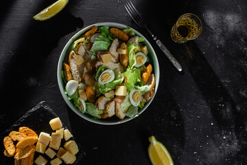Caesar salad with chicken in a plate on a dark background