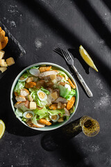 Caesar salad with chicken in a plate on a dark background
