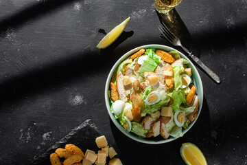 Caesar salad with chicken in a plate on a dark background