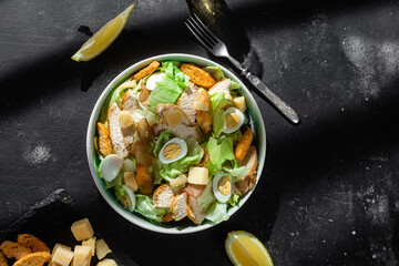 Caesar salad with chicken in a plate on a dark background