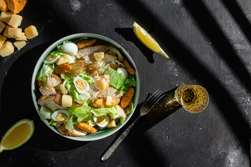 Caesar salad with chicken in a plate on a dark background