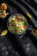 Caesar salad with chicken in a plate on a dark background
