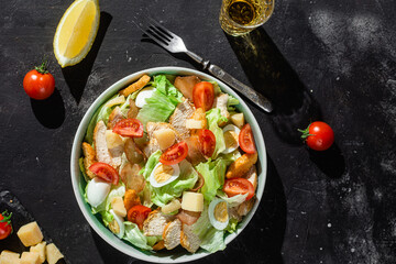 Caesar salad with chicken in a plate on a dark background