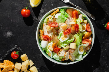 Caesar salad with chicken in a plate on a dark background