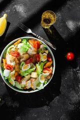 Caesar salad with chicken in a plate on a dark background