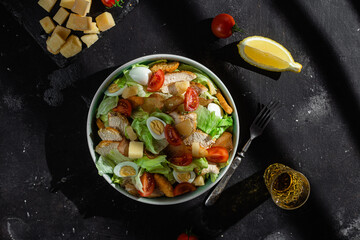 Caesar salad with chicken in a plate on a dark background