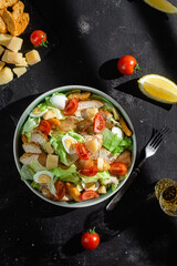 Caesar salad with chicken in a plate on a dark background