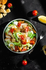 Caesar salad with chicken in a plate on a dark background