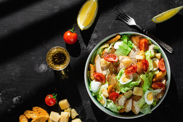 Caesar salad with chicken in a plate on a dark background