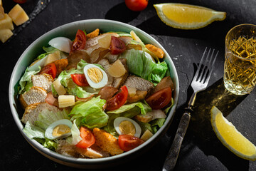 Caesar salad with chicken in a plate on a dark background