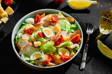 Caesar salad with chicken in a plate on a dark background