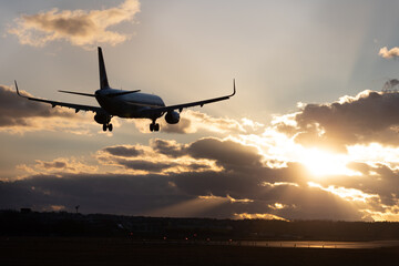 Aircraft landing at Stuttgart Airport, landing gear down, against golden sunset sky with some...
