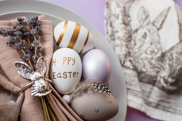 Banner. Table setting. A plate with a rabbit on a napkin, lavender and Easter eggs on a fashionable background of 2022 is a veri pery. Top view. The concept of a happy Easter holiday for cafes.