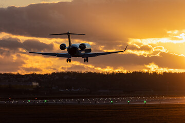 Aircraft landing at Stuttgart Airport, landing gear down, against golden sunset sky with some...
