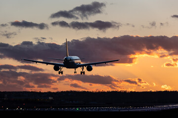 Fototapeta na wymiar Aircraft landing at Stuttgart Airport, landing gear down, against golden sunset sky with some clouds, partly blurred by heat of jet engines