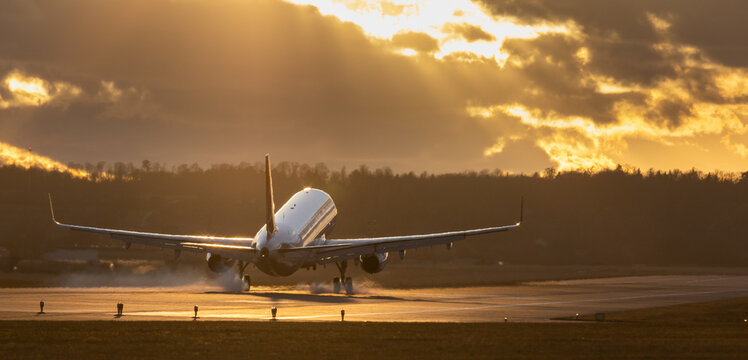 Aircraft landing at Stuttgart Airport, landing gear down, against golden sunset sky with some clouds, partly blurred by heat of jet engines
