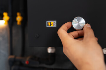 Male hand adjusting temperature on water gas heater of black colour.