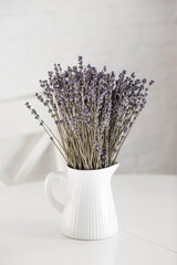 Provence. A beautiful bouquet of lavender in a white ceramic jug on the table. In the background is the interior of a modern white Scandinavian-style kitchen. The concept of home comfort.