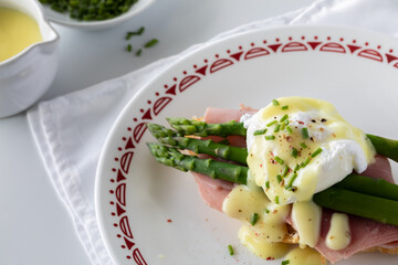 Close up of a plate of eggs benedict topped with hollandaise sauce and chives.