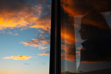 Silhouette of girl through glass of window on background of sunset sky.