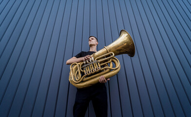 Young street musician playing the tuba near the big blue wall