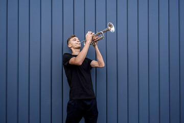Young street musician playing the trumpet near the big blue wall