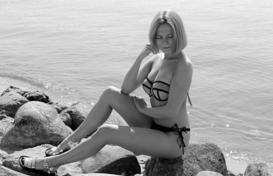One girl in swimsuit sits on stone. Cute girls with sporty figures. Black and white photo.