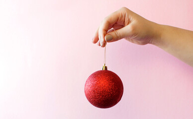 Christmas concept with hand and red ball - christmas tree toy. Red round christmas ball in female hand on pink background. New Year holidays celebration decoration.