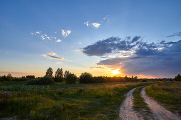 Scenic countryside landscape with rural dirt road at sunset in Russia. Summer beautiful sunset in the meadows with a rural road.
