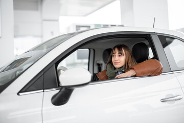 Portrait of a confident young woman sitting on the driver's seat of her white car at gas station....