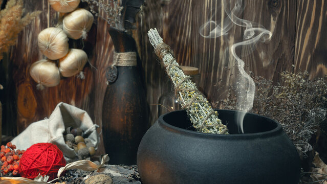 Pagan Witch Magic Altar. Smoking Twist Of Bitter Wormwood Herb For Fumigation In Cast Iron Cauldron, Ritual Objects In Wooden Background, Dark Key, Selective Focus.