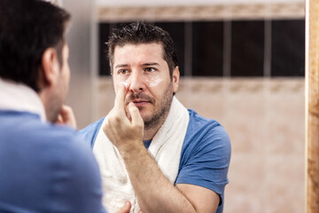 Portrait of mature man applying anti aging cream under eyes - 488376063