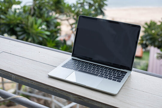 Laptop on a wooden table and trees with nature background.