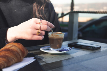 Young caucasian woman talking by phone while taking a coffee and croisant at a terrace.