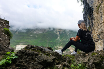 A girl on the background of a mountain landscape in the clouds. Stone bowl in Dagestan. Russia