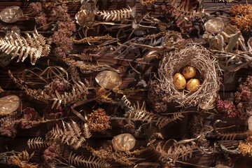 golden quail eggs in nest with dried flowers on dark wooden background