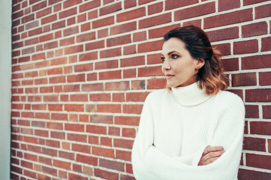Romantic woman looking away with nostalgia against a brick wall