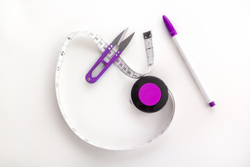 Tailor's tape measure with a thread cutter and a marker on a white background. View from above