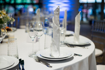 A festively served table inside the restaurant. Rolled-up tissues standing on the plates. A candle on the table. Wedding banquet.