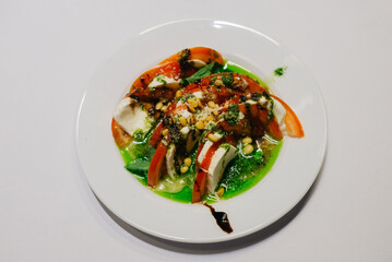 A portion of caprese on a white plate on a white table. A traditional Italian starter of mozzarella cheese, with fresh tomatoes, pesto sauce and balsamic sauce.