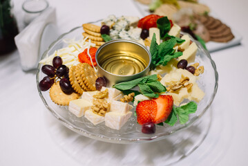 Glass plate with appetizers on the banquet table. Cheeses, walnuts, honey, grapes, mint leaves