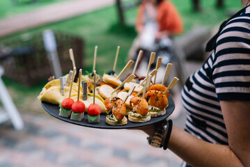 Waitress in holding a plate with canapes. Catering service. Wedding welcome food..Сanapes (shrimp, mozzarella, sun-dried tomatoes). Welcome buffet at the event.