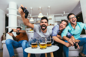 Smiling male friends with gamepads and beer playing video game at home