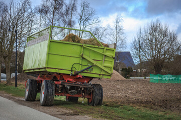 Obraz premium green tractor trailer stands on the roadside next to a field.