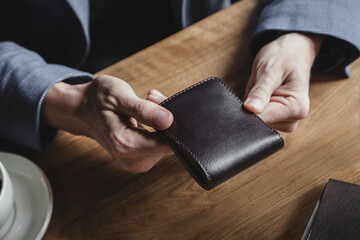A business man at a wooden table holds a leather wallet in a cafe and waits for a lunch bill. No face, close-up - obrazy, fototapety, plakaty
